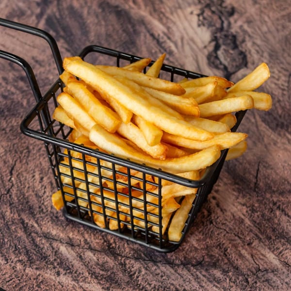 Golden-brown french fries piled high in a black wire basket on a rustic wooden surface.