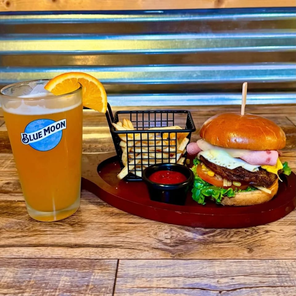 A burger with fries and a Blue Moon beer with an orange slice on a wooden table.