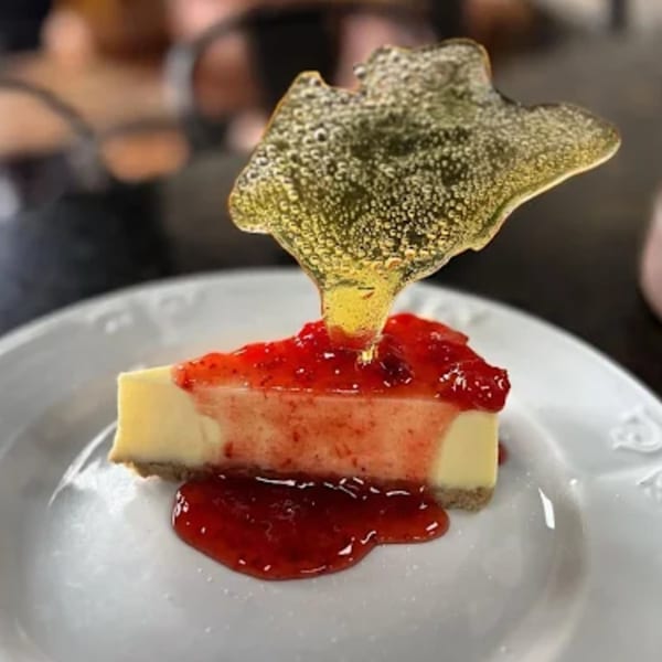 Cheesecake slice with strawberry topping and a decorative sugar shard on a white plate.