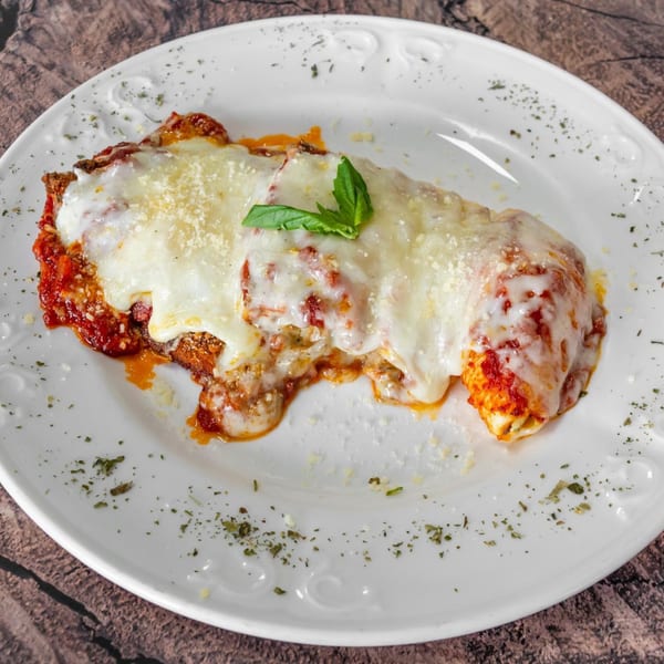 Baked ziti with melted mozzarella, red sauce, and fresh basil on a white plate.