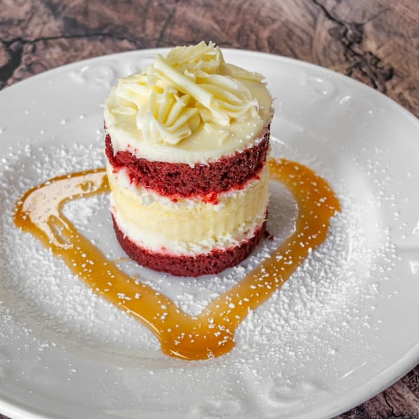Layered red velvet and vanilla cake with white frosting, caramel, and powdered sugar on a white plate.