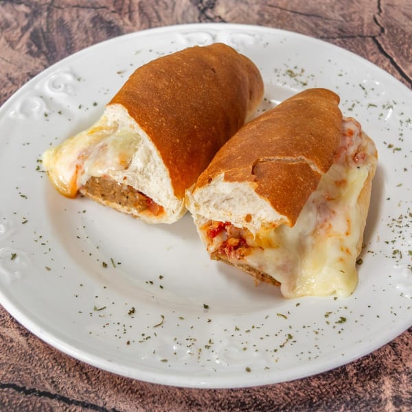 Two halves of a meatball sub sandwich with melted cheese and sauce on a white plate.