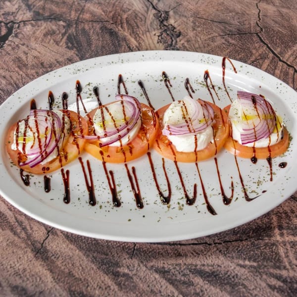 Four slices of tomato topped with mozzarella, red onion, olive oil, and balsamic glaze.